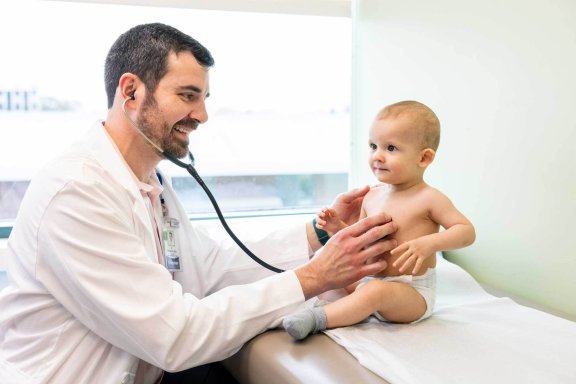 Male pediatrician checks heart beat of baby