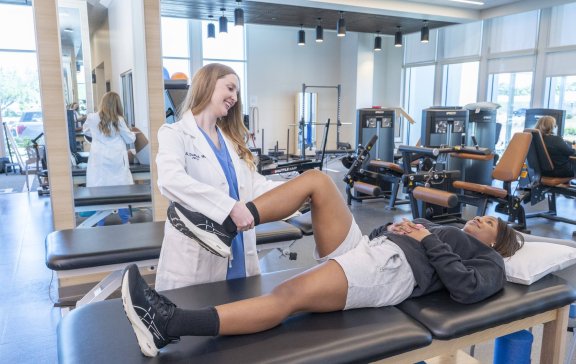 Doctor helping patient move leg on physical therapy table