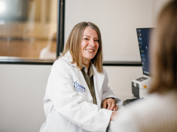Doctor wearing white coat smiling at patient while using a computer