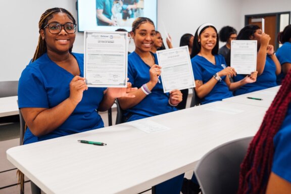 LAUNCH 2 Students in blue scrubs at table holding up letters