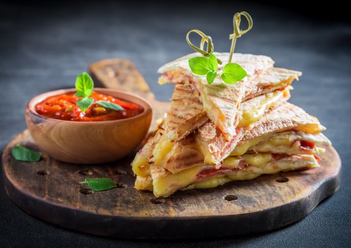 Healthy breakfast quesadilla cut up on a wooden plate with salsa on the side