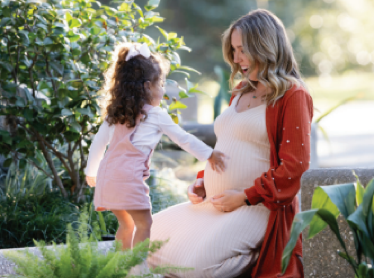 Daughter touching pregnant moms belly kneeling