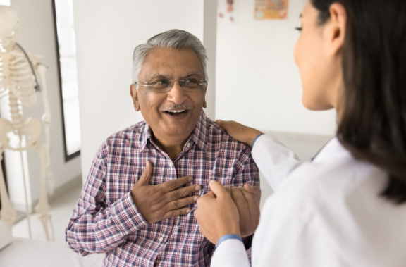Older man with hand over his heart smiling at doctor