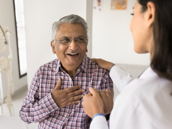 Older man with hand over his heart smiling at doctor