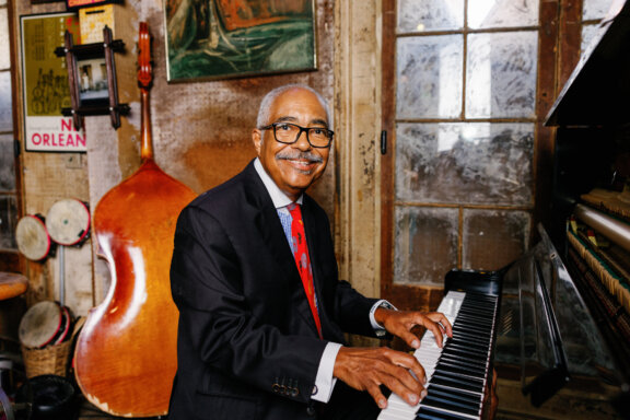 Rickie Monie sitting at a piano smiling