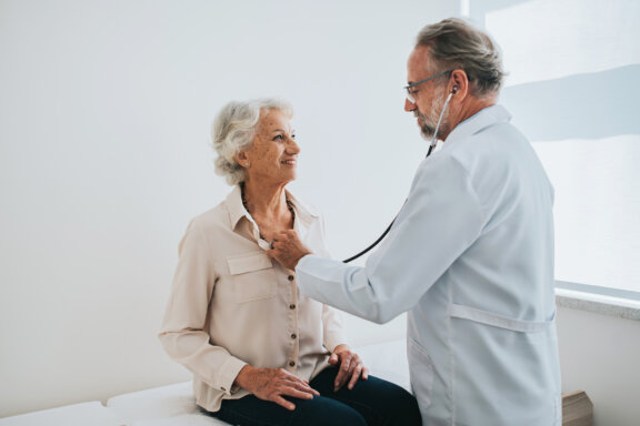 Cardiac surgeon listening to patients heart in exam room.