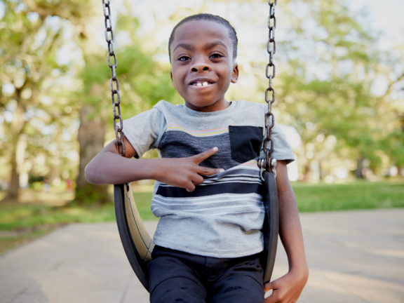 Little boy in swing smiling and doing a peace sign
