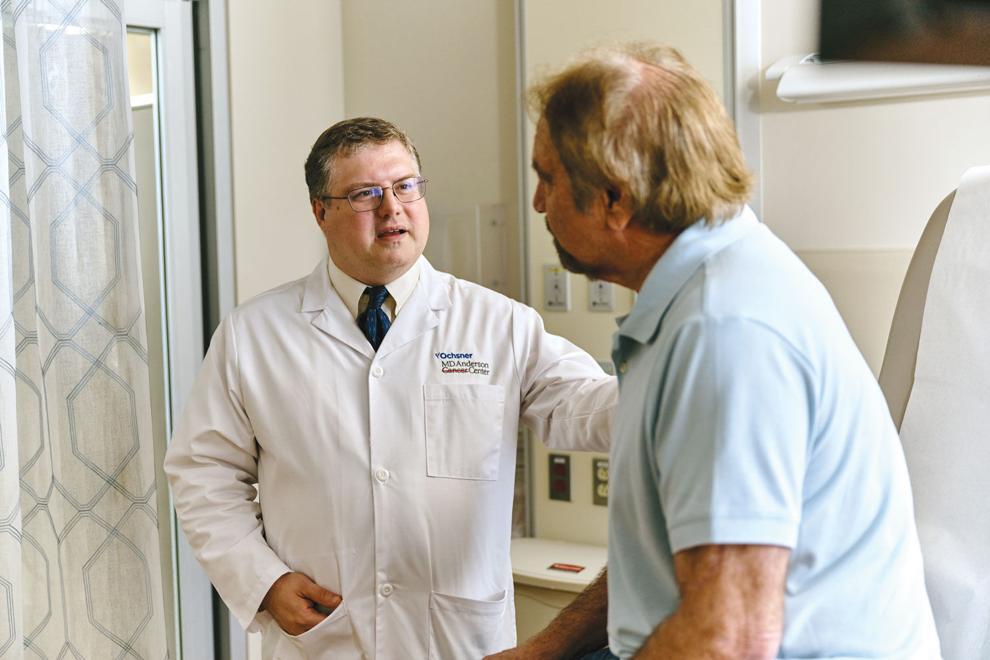 Marc R. Matrana, MD in a white lab coat with an Ochsner MD Anderson Cancer Center logo speaking with and placing a hand on the shoulder of a male patient sitting on an examination table.