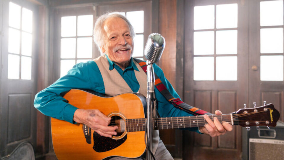 man in blue shirt smiling, holding guitar