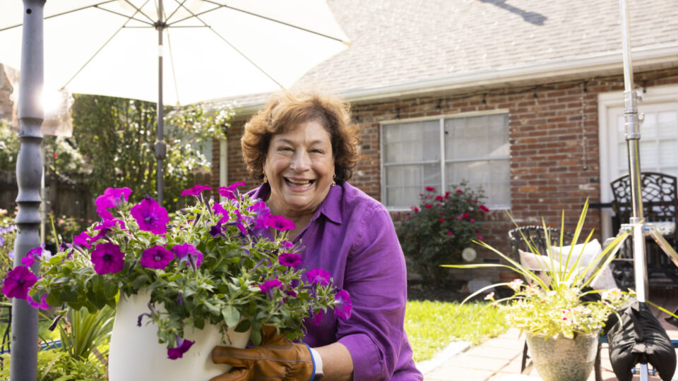 woman holding pot of purple flowers smiling at camera