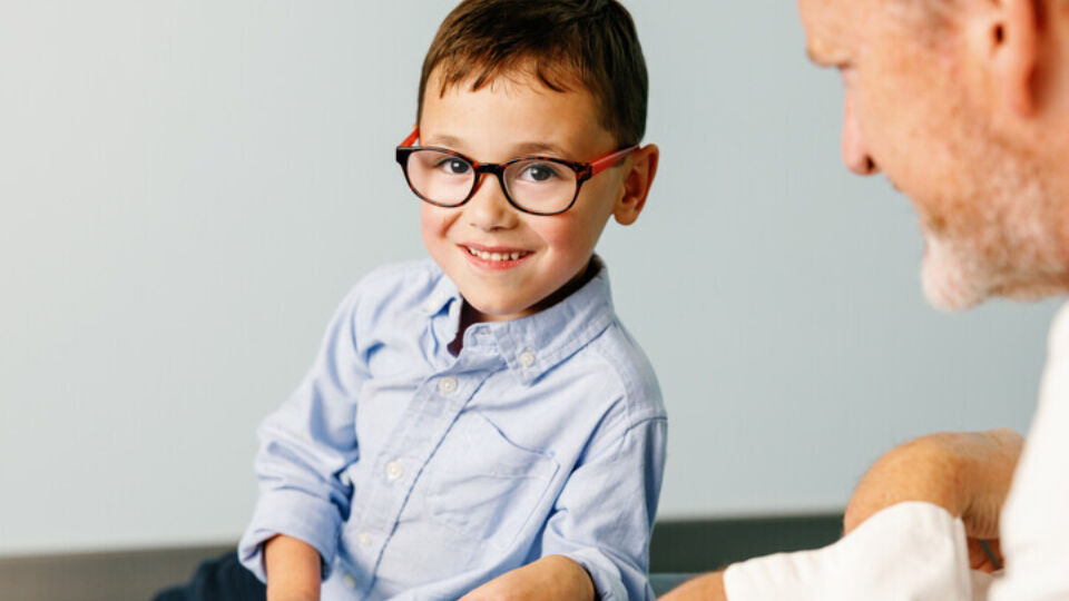 little boy in glasses smiling with pediatric heart surgeon